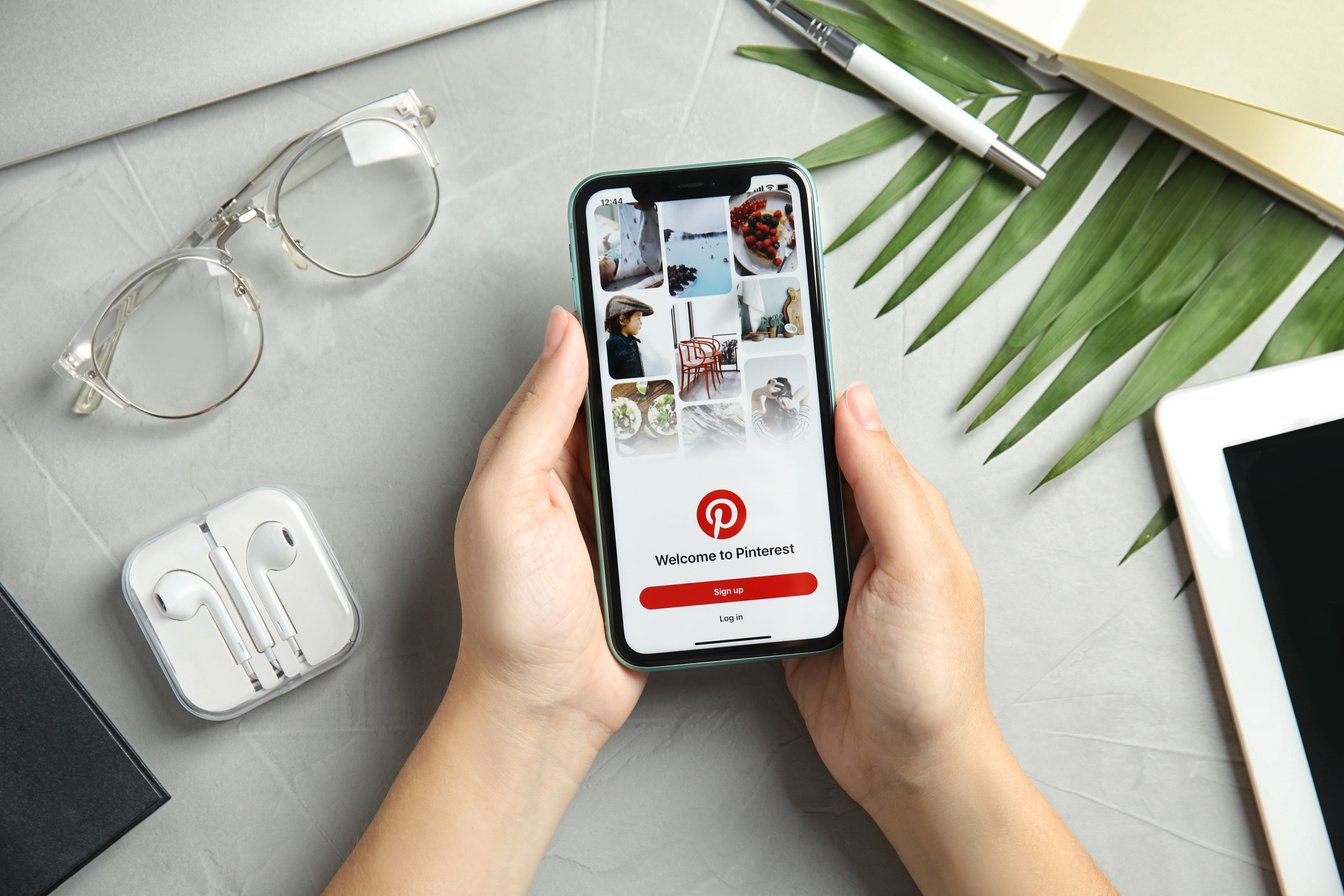 MYKOLAIV, UKRAINE - JULY 9, 2020: Woman Holding Iphone 11 with Pinterest App on Screen at Grey Table, Top View