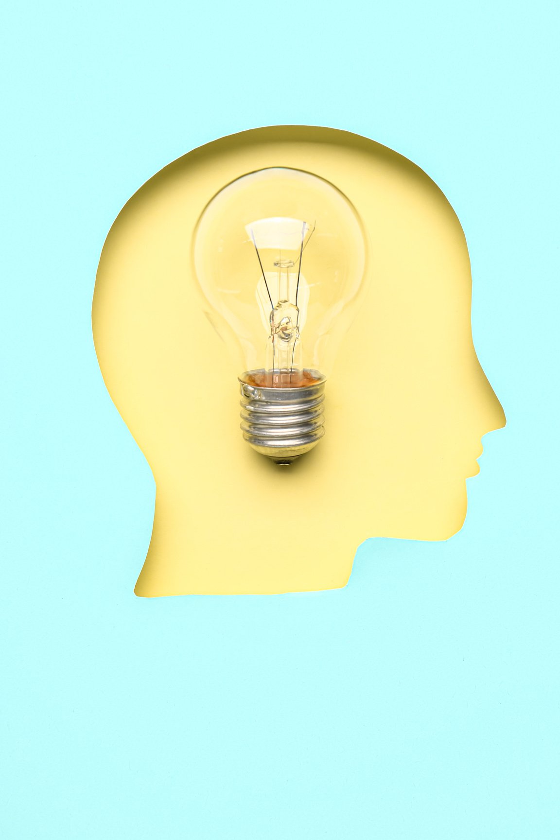 Light Bulb Visible through Cut Blue Paper in Shape of Human Head on Yellow Background